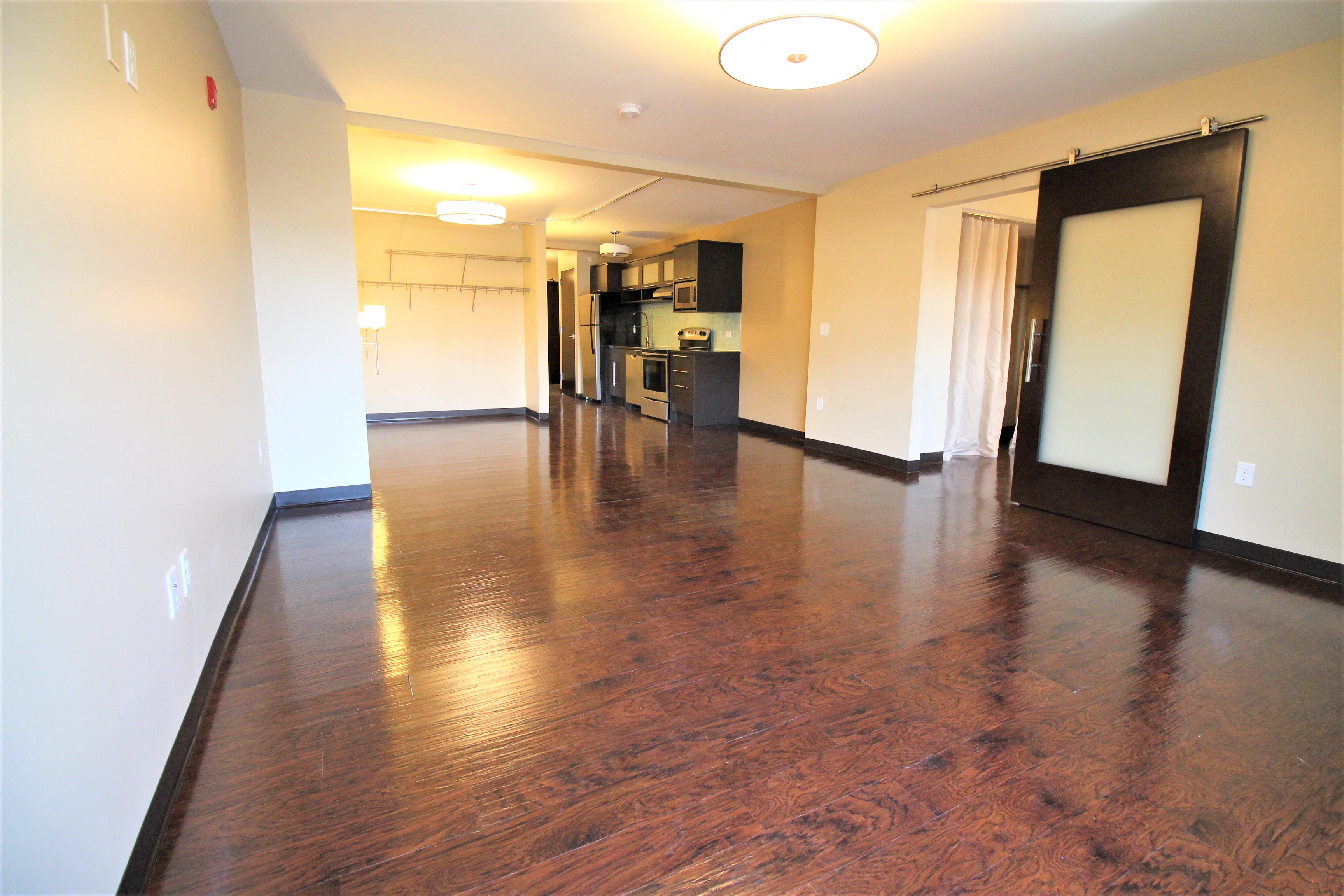 an empty living room with wood floors and a door to a kitchen
