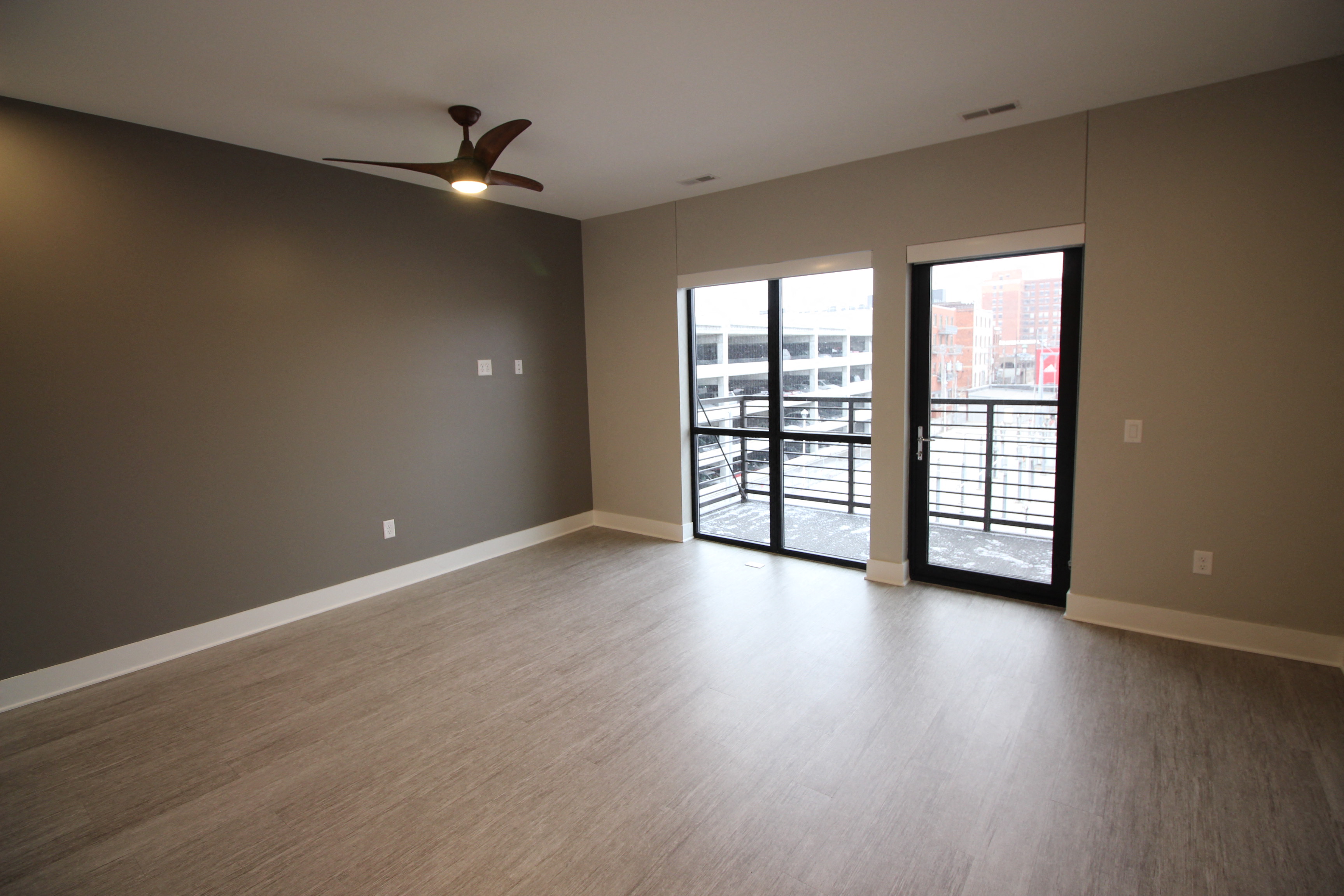 an empty living room with a ceiling fan and a balcony