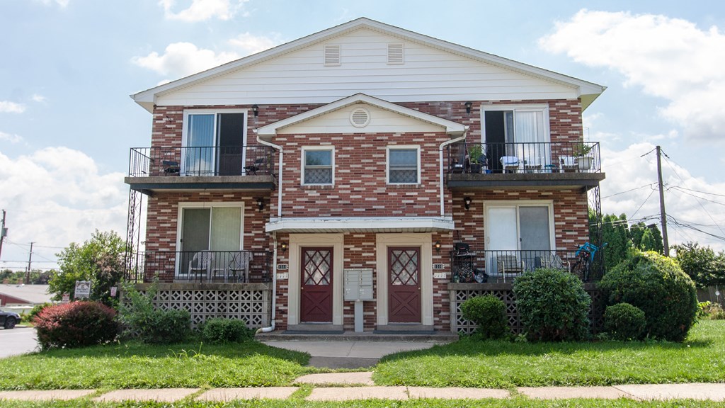 the front of a brick house with a porch and a lawn