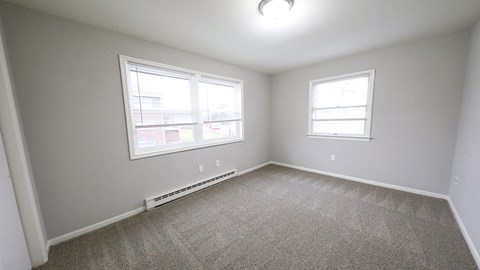 an empty bedroom with two windows and carpeting