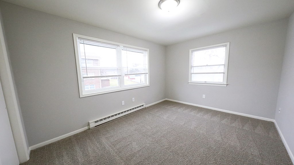 an empty bedroom with two windows and carpeting