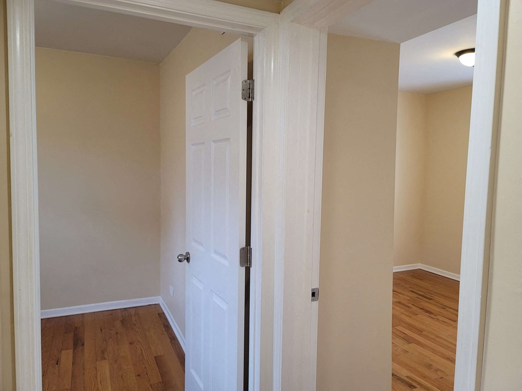 a bedroom with a white door and a hallway with wood floors