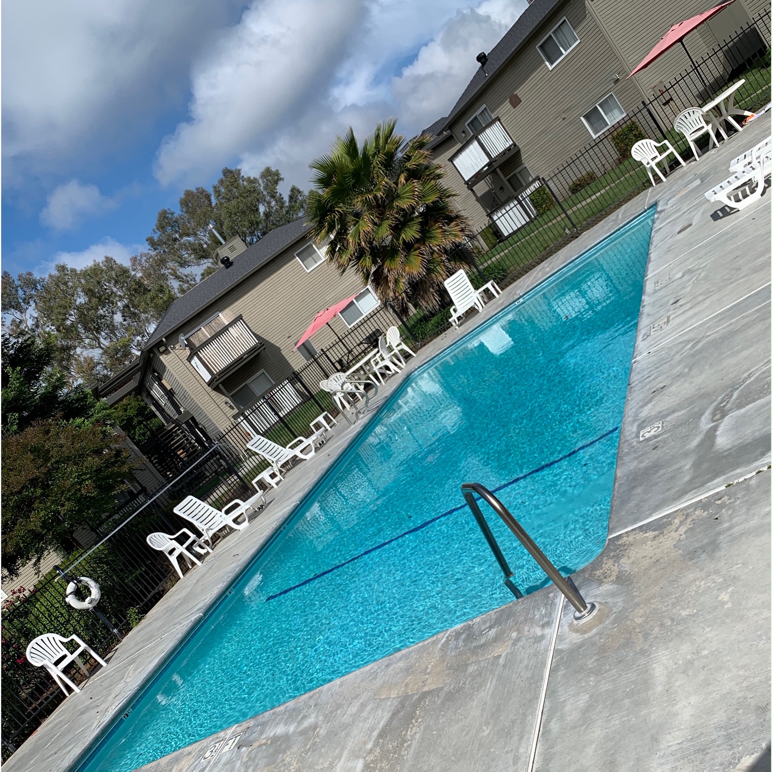 A swimming pool with a diving board and white chairs.