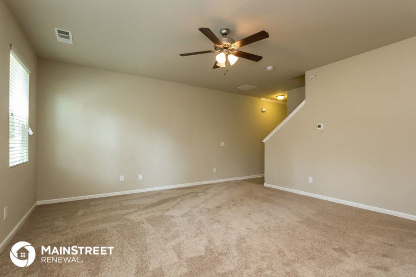 the spacious living room with carpeted flooring and ceiling fan