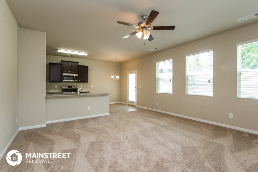 an empty living room with a ceiling fan and a kitchen
