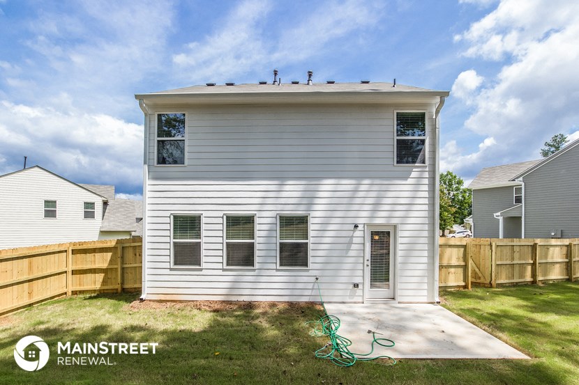 the backyard of a small white house with a wood fence