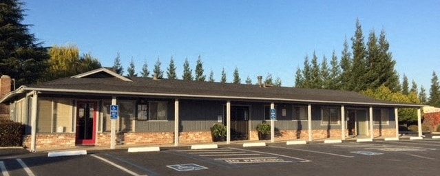 the front of a building with a parking lot and trees