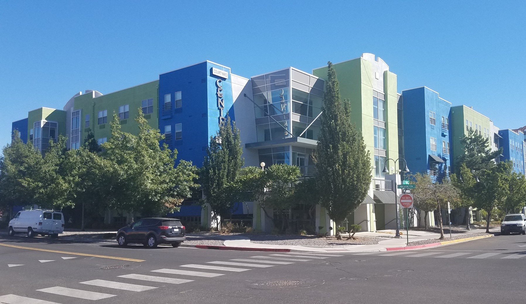 A street view of a modern building with cars and trees.