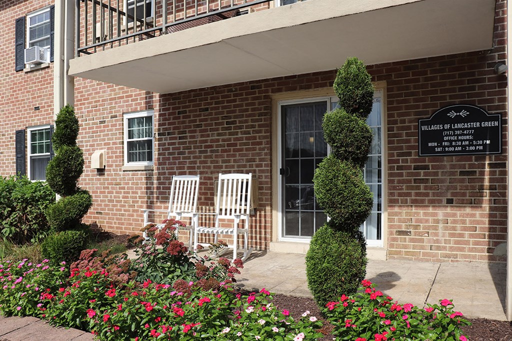 the front of a brick building with flowers and a sculpted tree in front