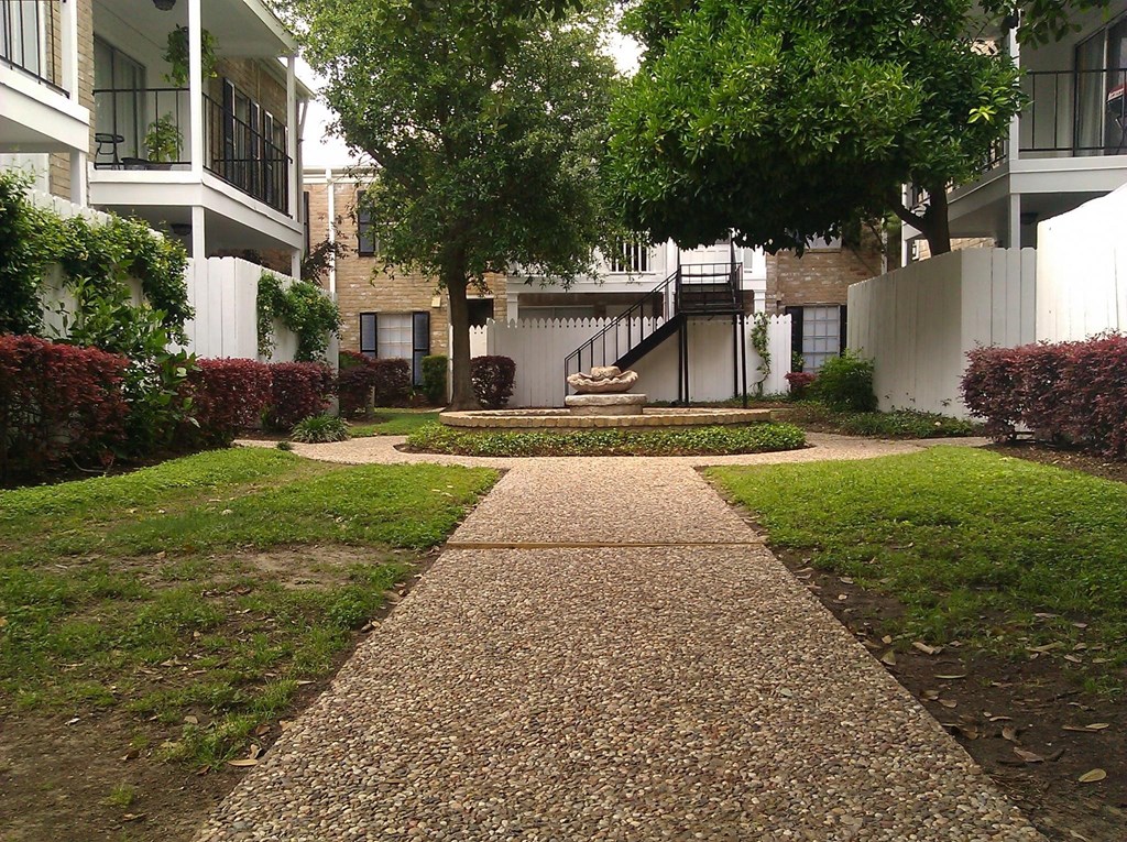 a walkway leading to an apartment building with trees and grass