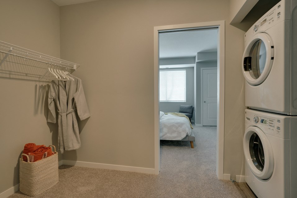 a washer and dryer in a laundry room with a bedroom in the background