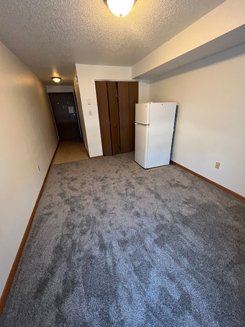 A white refrigerator sits in a room with a carpeted floor.