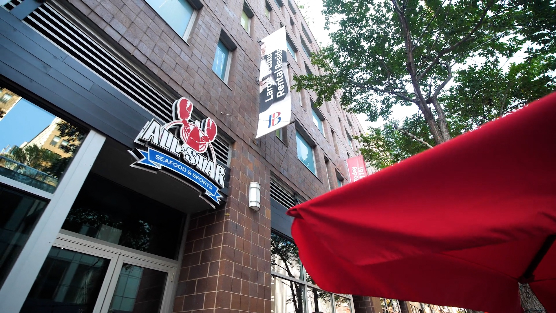 Looking up at the Allstar Seafood & Sports sign above the entry door. There is a red café umbrella peaking into the picture from the right.