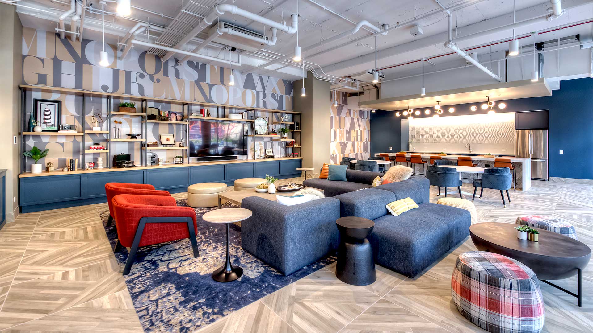 A collection of comfortable chairs and sofas sits in the middle of the room. The back wall to the left is a large bookshelf with a variety of objects on it and a large television.