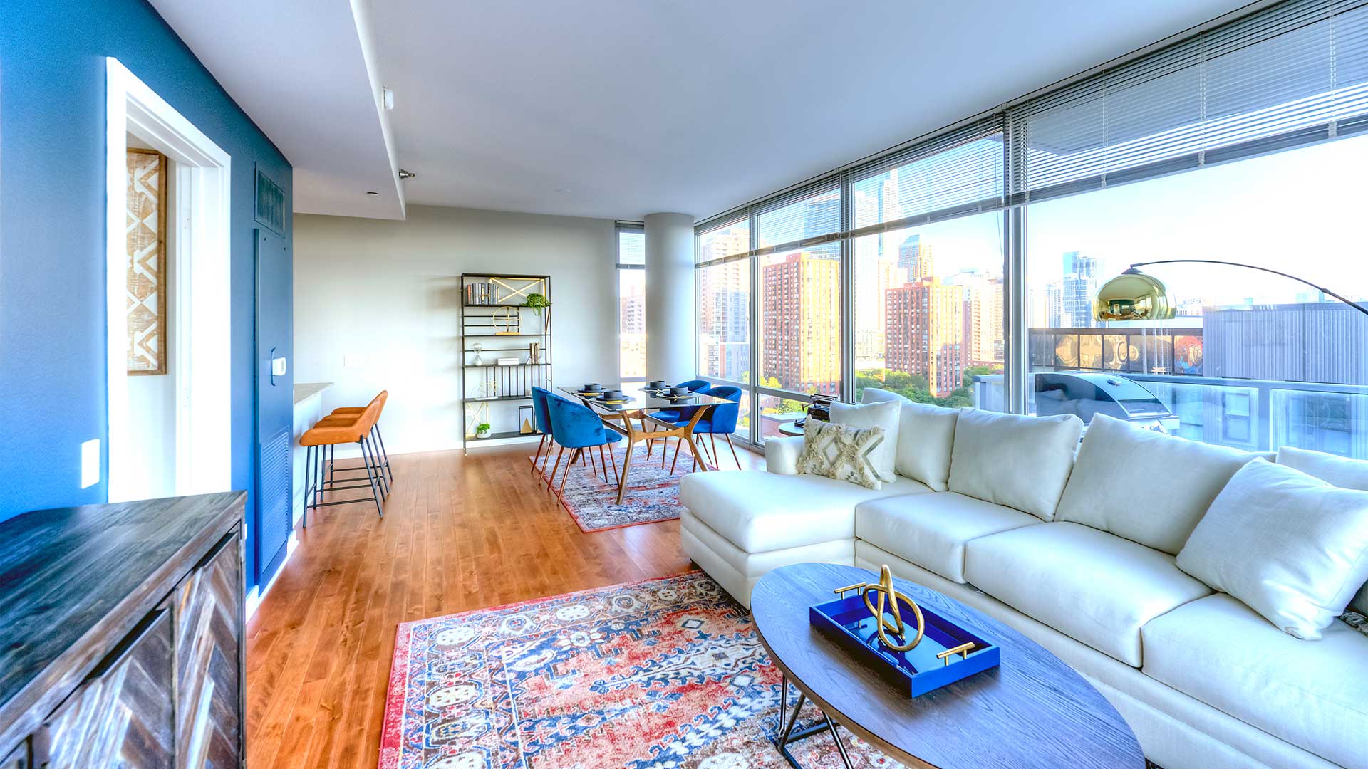 Looking down a living/dining room in a residence at Burnham Pointe. A couch is close on the right with a dining further down along the windows. To the left is a doorway to the bedroom and further down