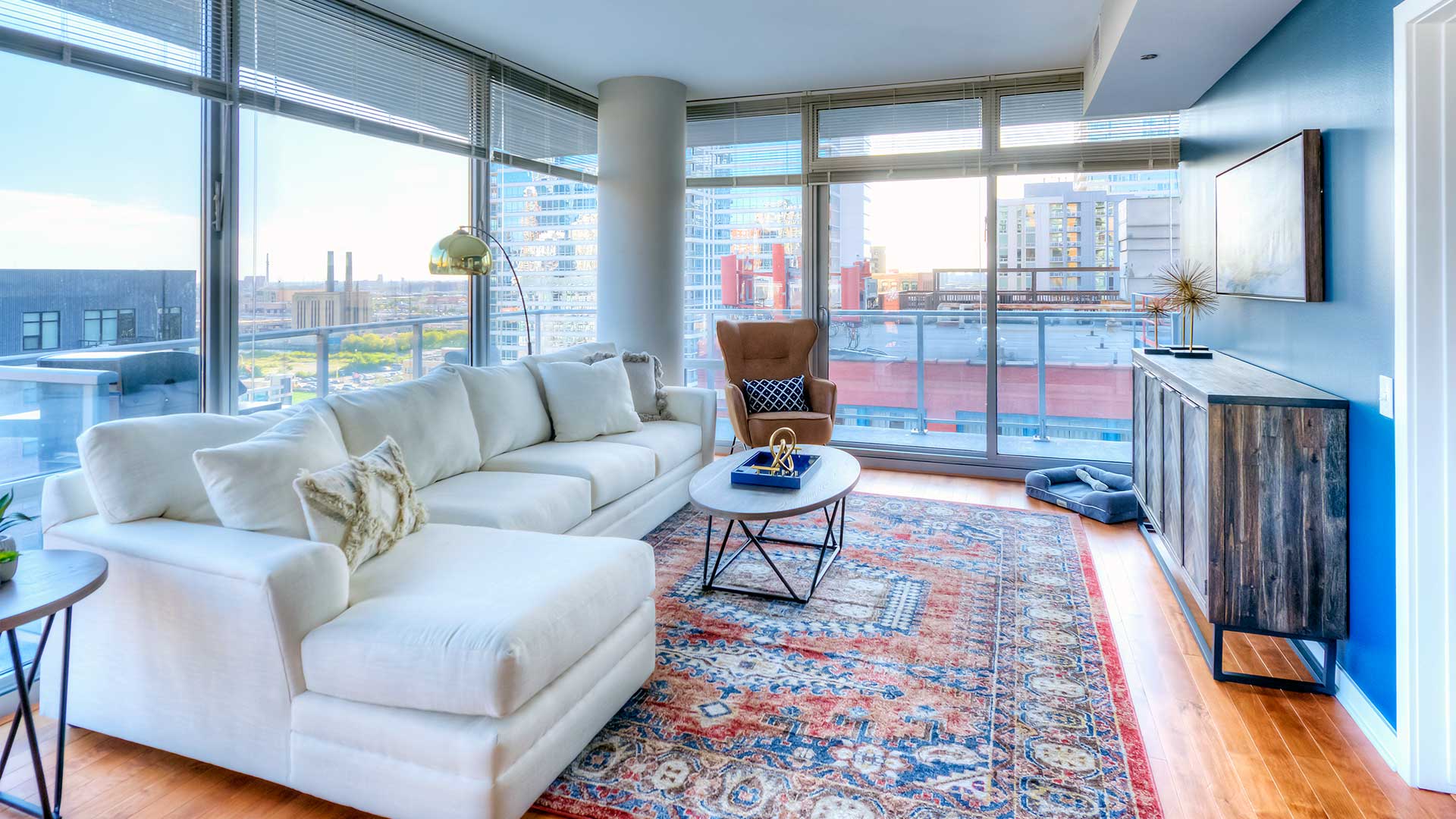 Looking into a living in a Burnham Pointe residence. Floor-to-ceiling windows line the left and far walls with a couch and chair in front. The right wall has a cabinet along the wall.
