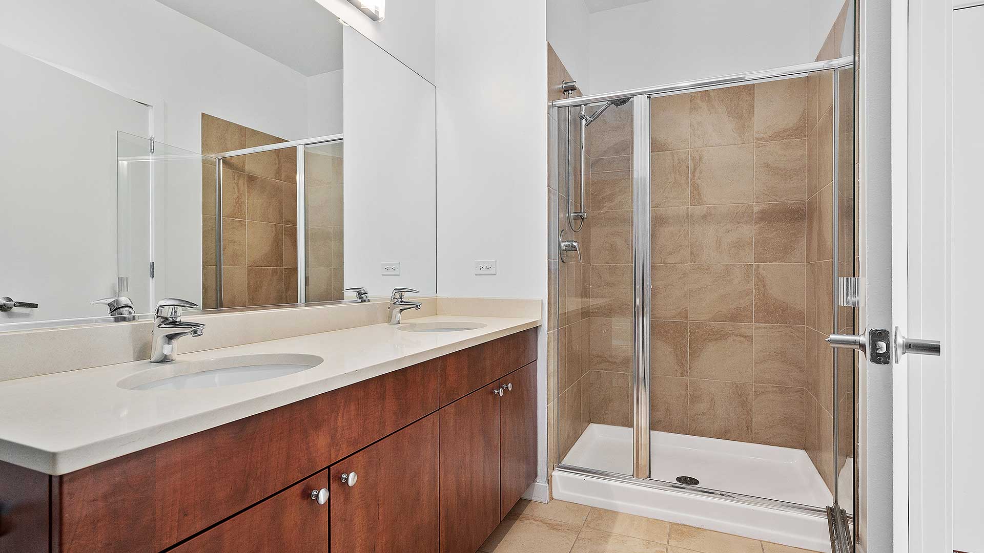 Looking into a bathroom in a Burnham Pointe residence. The vanity runs along the left leading to a walk-in shower on the far wall.