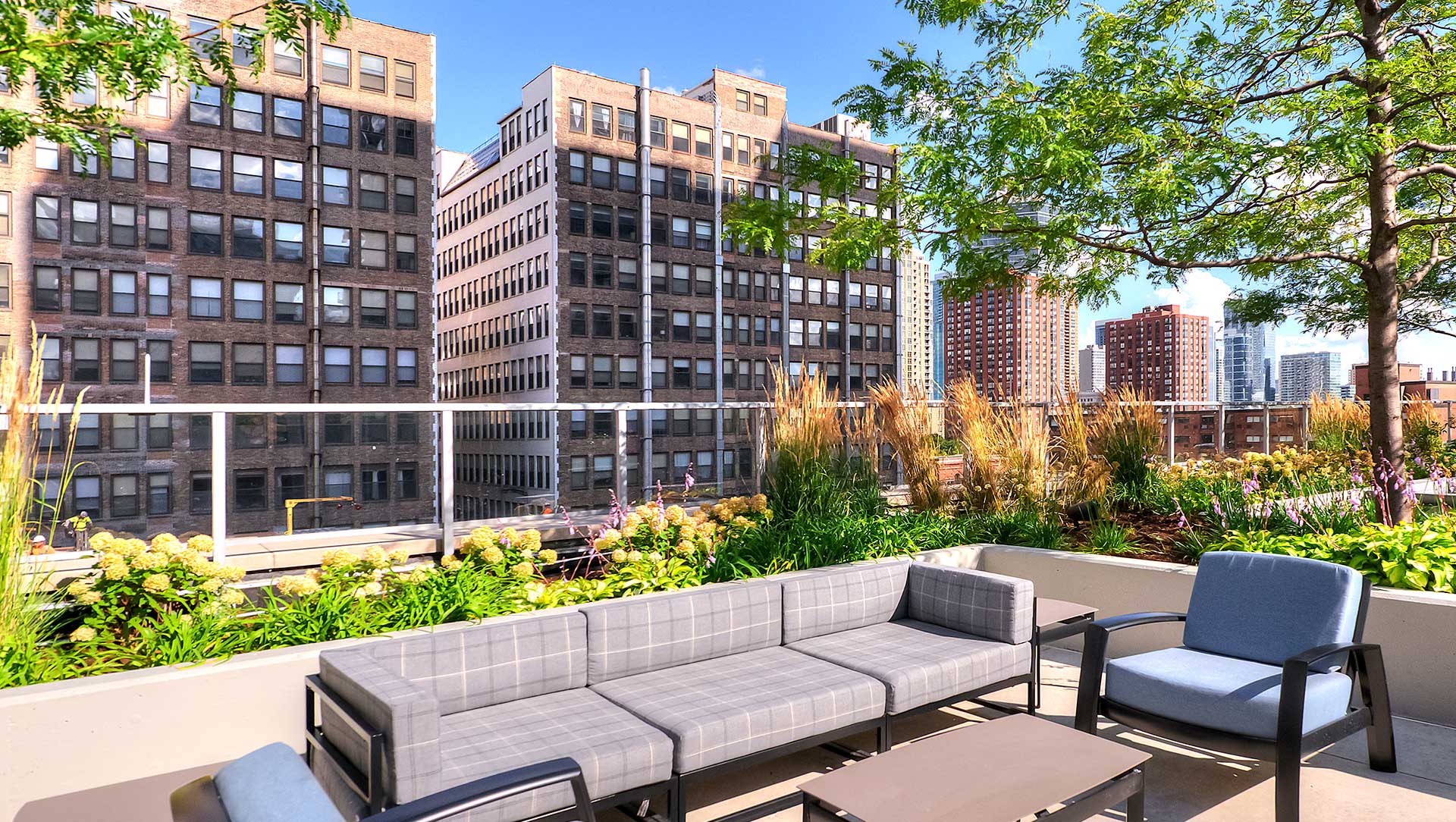 Looking out off the outdoor terrace at Burnham Pointe and the brick skyscrapers across the way. An outdoor couch is in the foreground with potted plants all around.