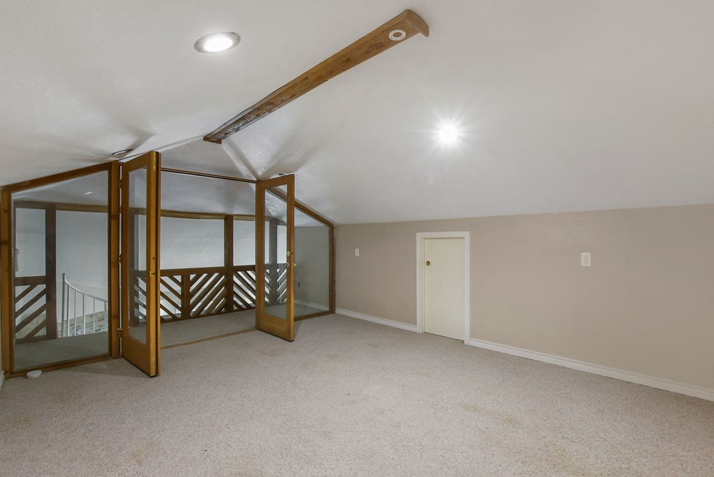 a bonus room with carpet and a mirrored closet and a staircase