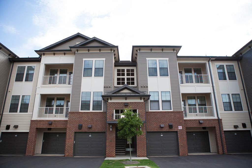 Luxury Apartments for Rent in Greenville SC - Velo Verdae - Property Exterior with Brick, White, and Tan Walls, Showcasing Balcony, Street, Garages, and Planted Tree