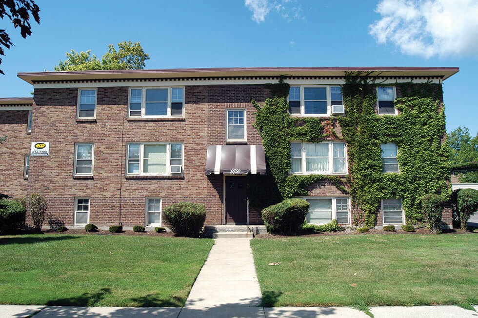 the front of a brick apartment building with a sidewalk and grass