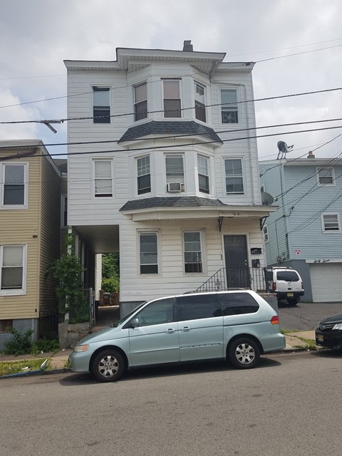 A blue car is parked in front of a two-story house.