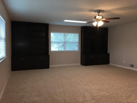 an empty living room with a ceiling fan and black cabinets