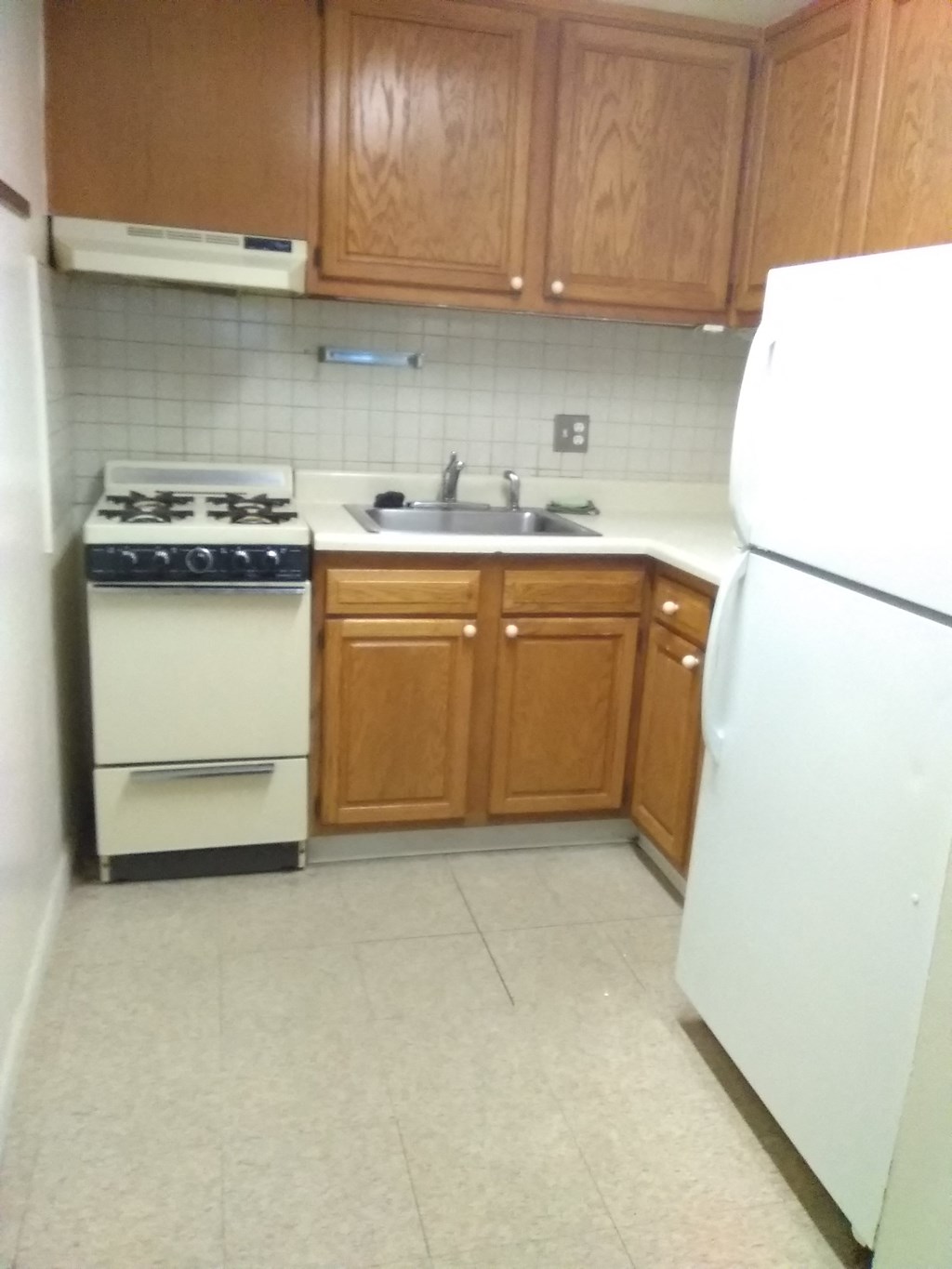 an empty kitchen with white appliances and wooden cabinets
