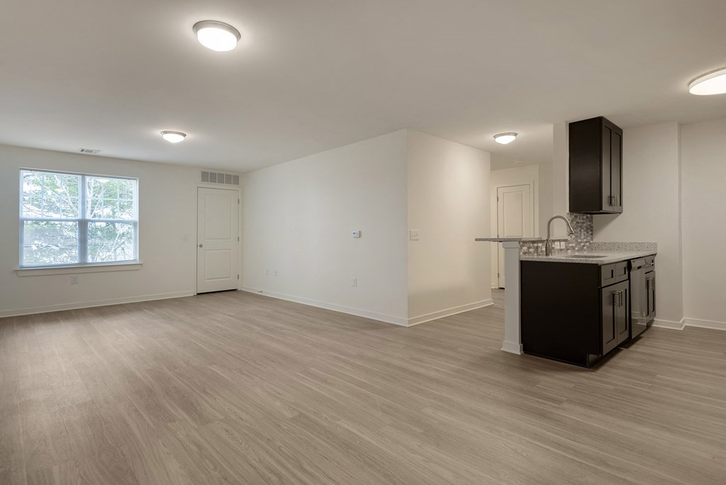 an empty living room with a kitchen and a window