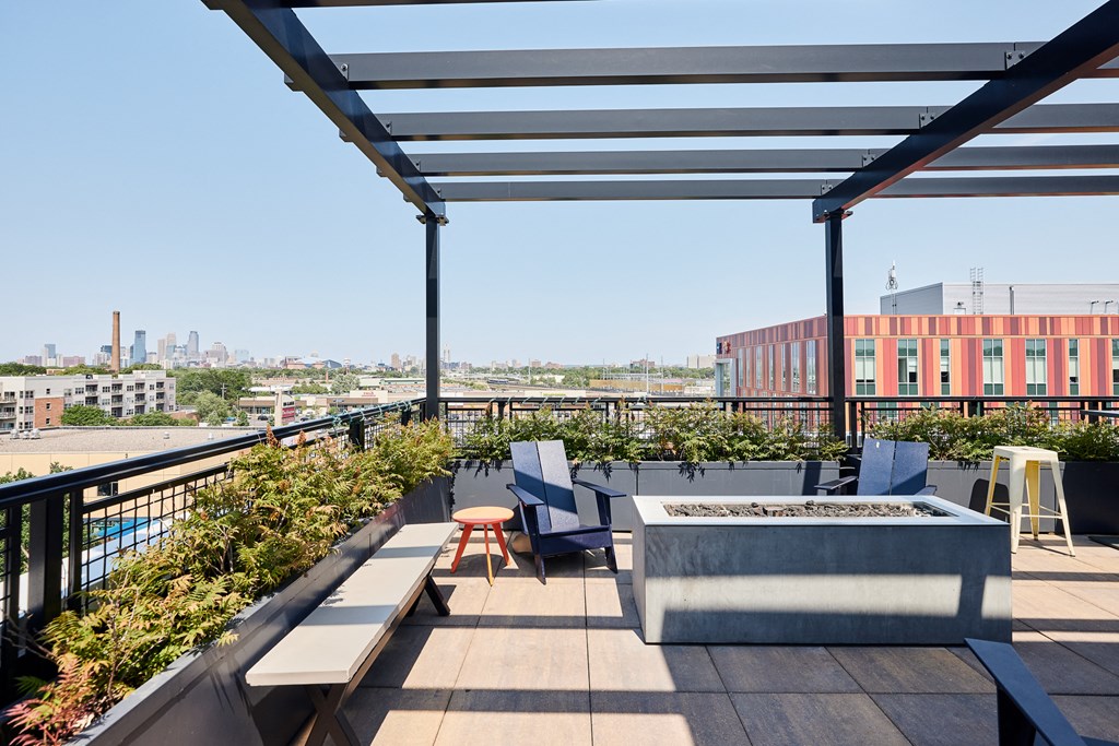 a rooftop patio with furniture and a fire pit and a city in the background