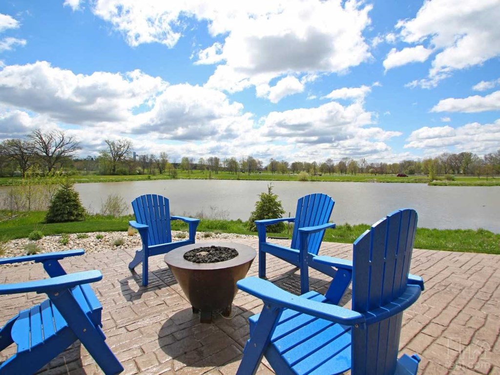 a patio with blue chairs and a fire pit overlooking a lake