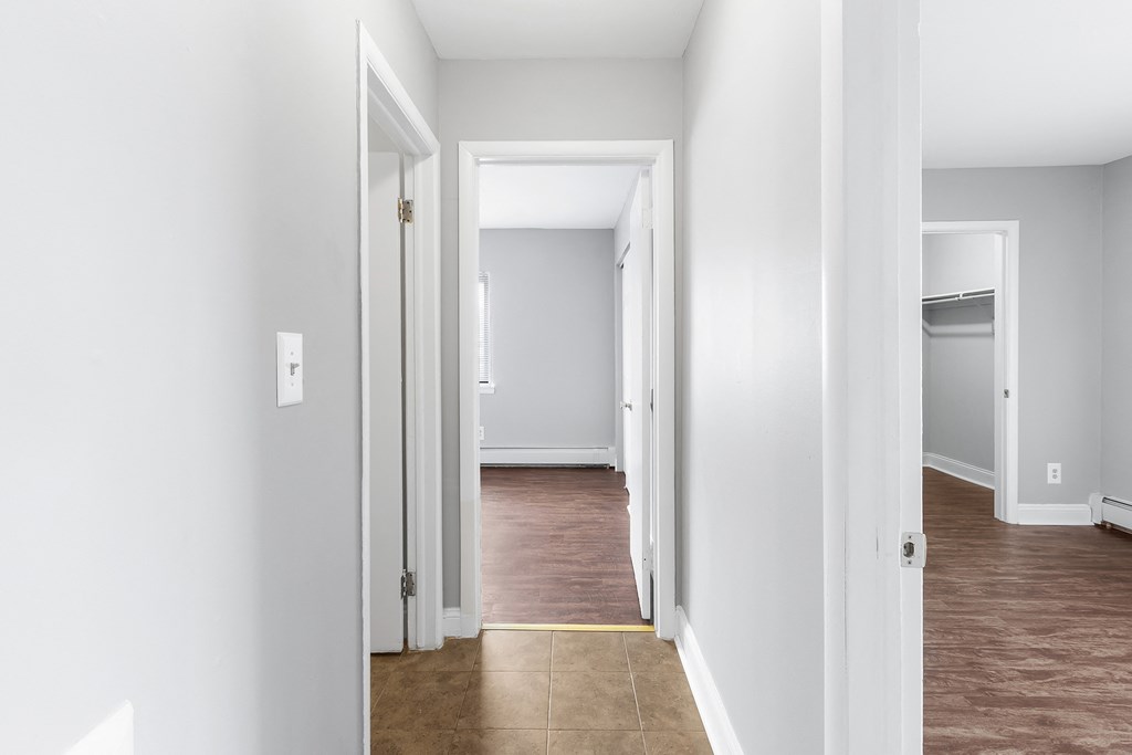 a hallway with a wood floor and white walls and a door to a bedroom