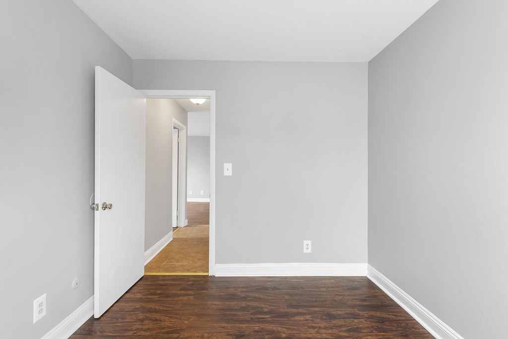 an empty room with white walls and wood flooring and a door to a hallway