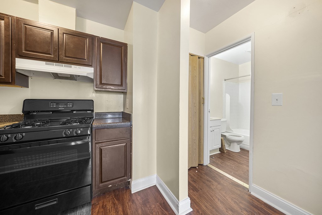 a kitchen with black appliances and wood flooring and a door to the bathroom