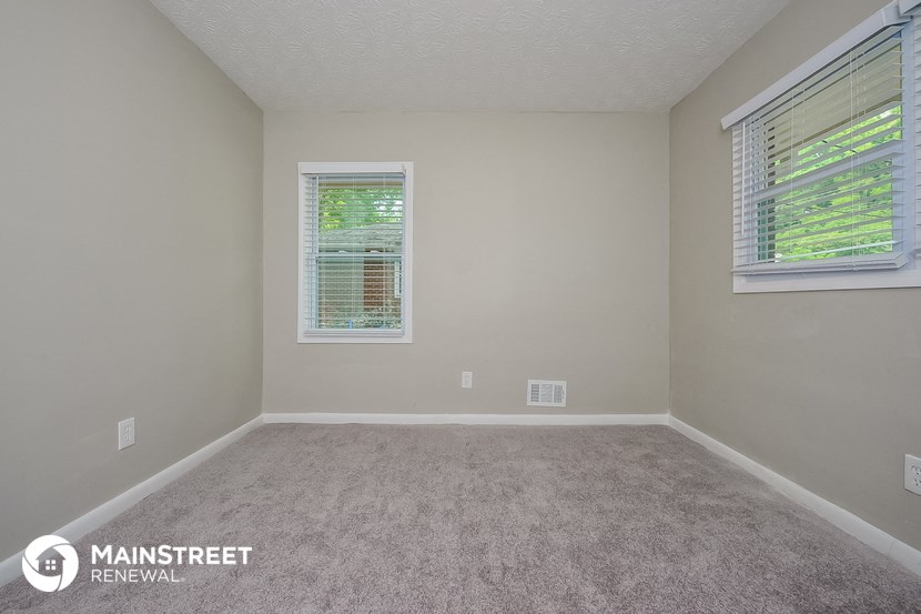 an empty room with a carpeted floor and two windows
