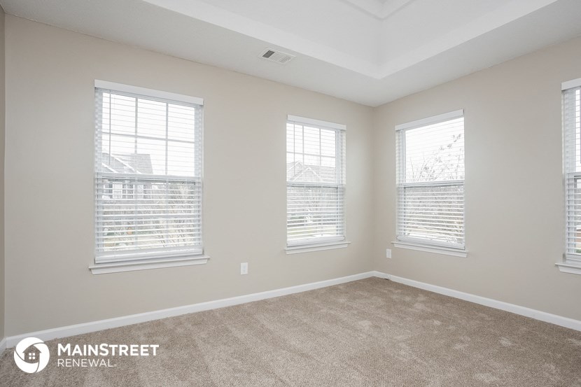 the living room of a new home with a carpet and three windows