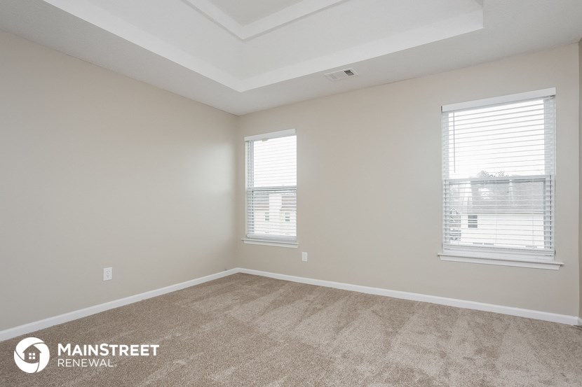 the living room of an apartment with carpet and two windows