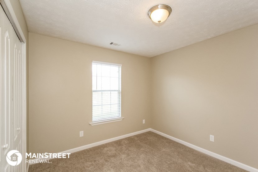the spacious bedroom with carpeted flooring and a window