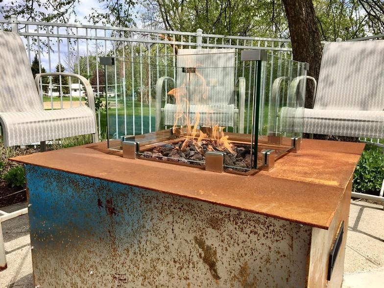 a fire pit in front of a fence and chairs