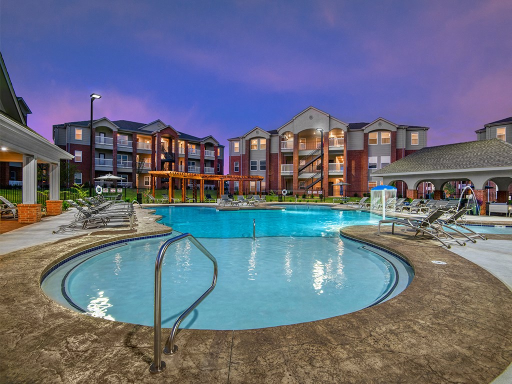 a swimming pool with chairs around it in front of an apartment building