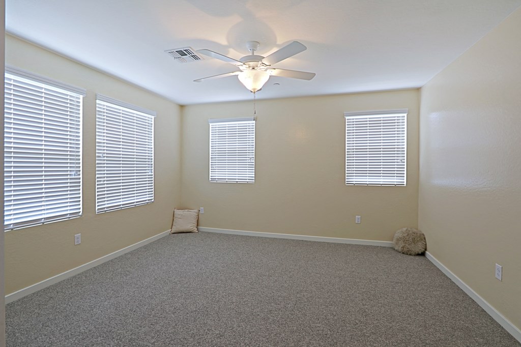 an empty room with a ceiling fan and three windows