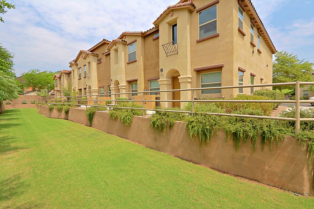 a row of apartments with a green lawn and a fence