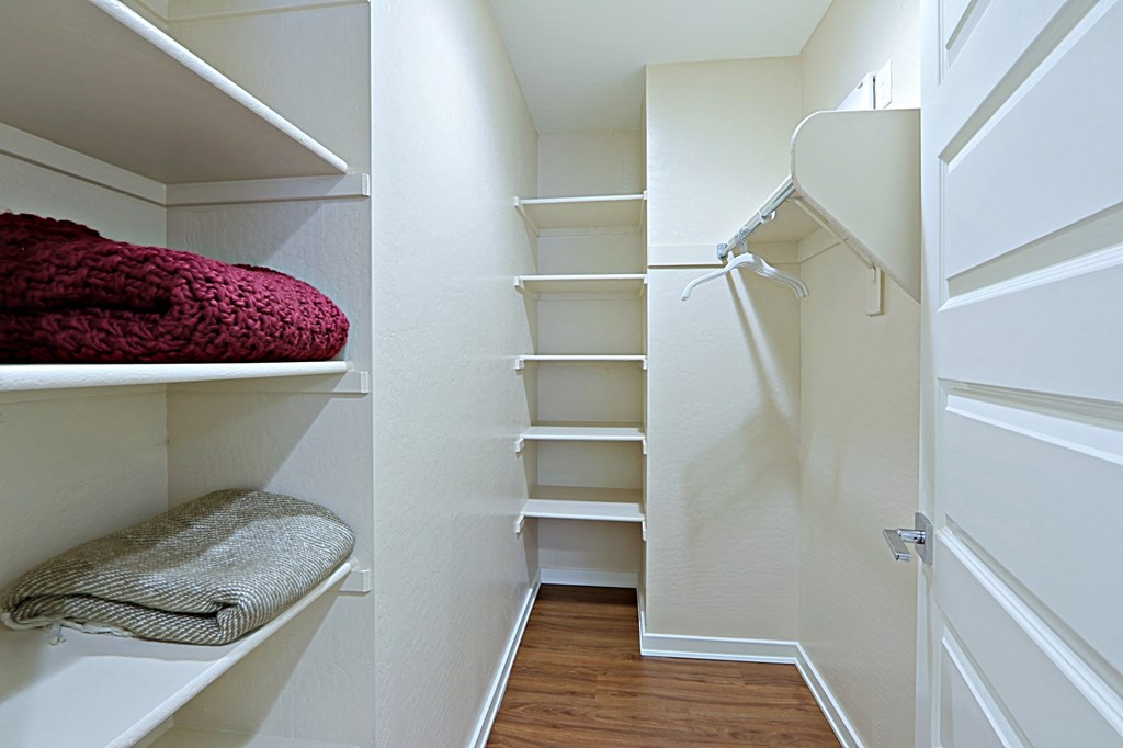 a walk in closet with white walls and shelves and a white closet door