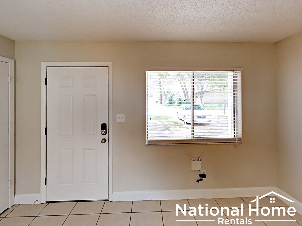 A white door is on the left and a window with blinds is on the right in a room with a white ceiling.
