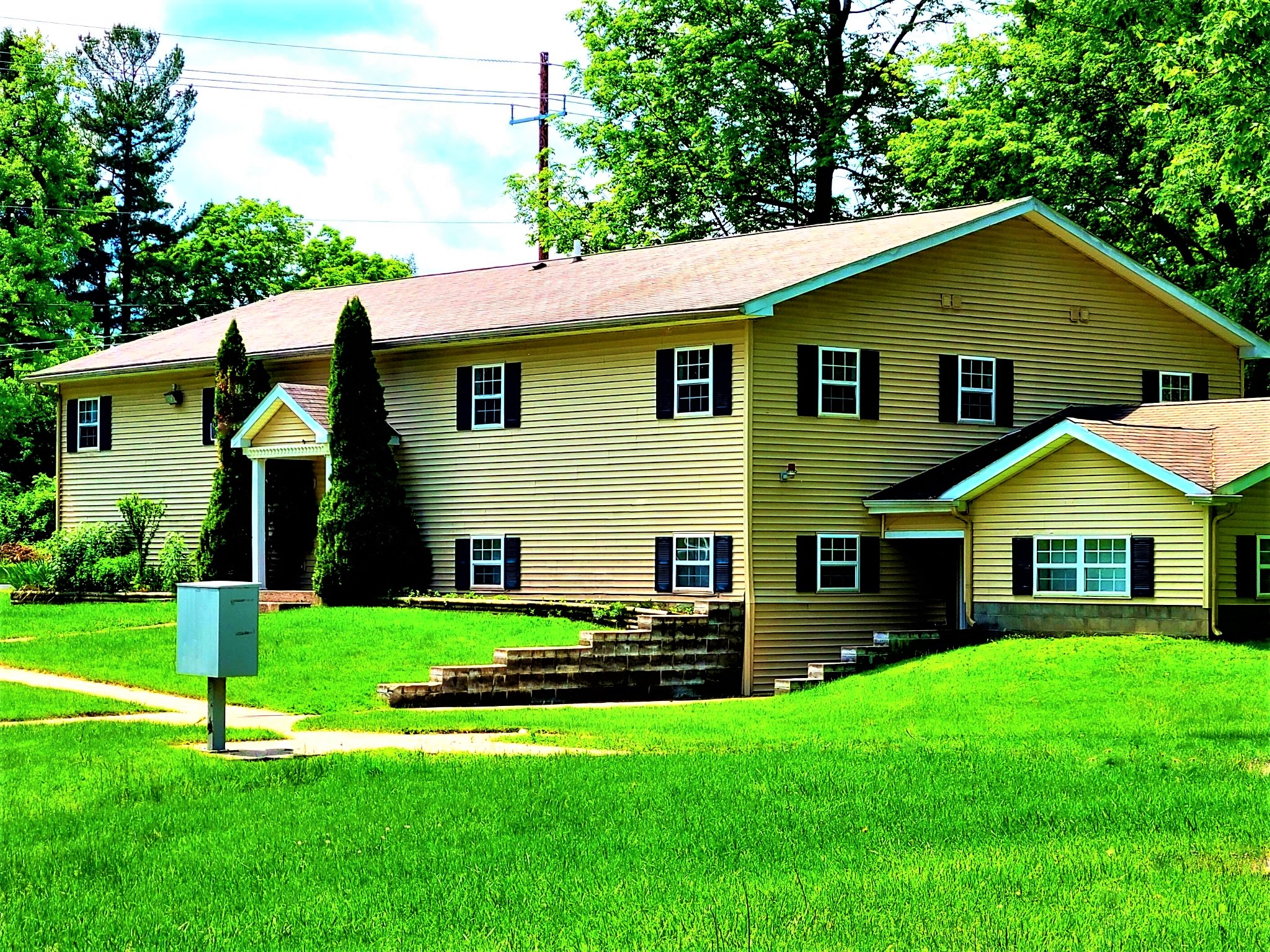 a yellow house with a green lawn and trees