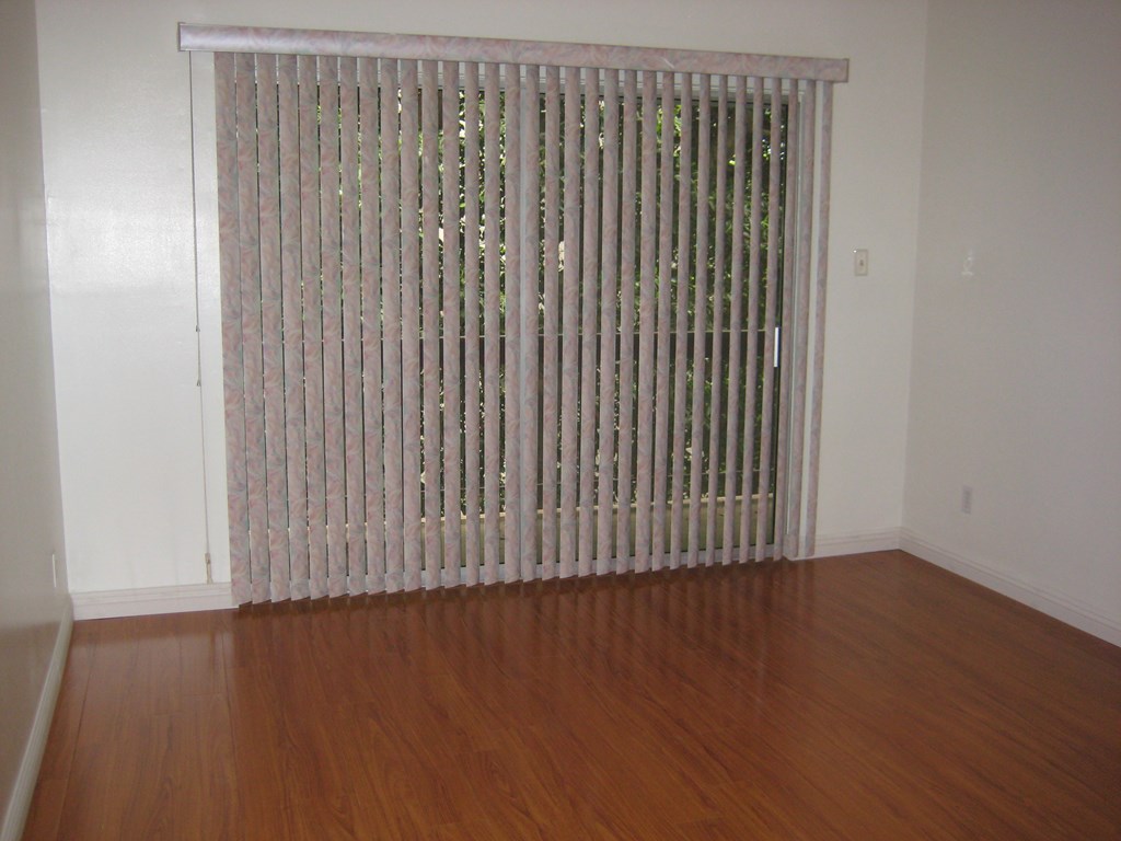 a living room with wood floors and a large window with white blinds