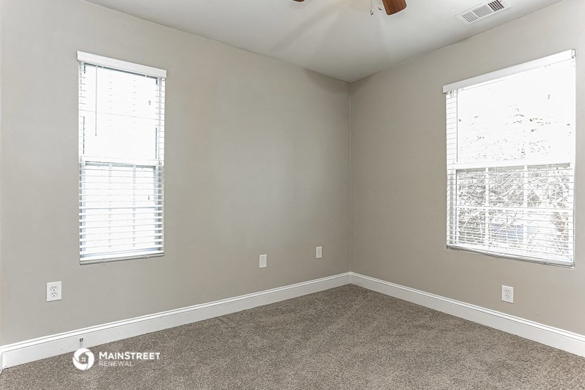 an empty room with two windows and a carpet