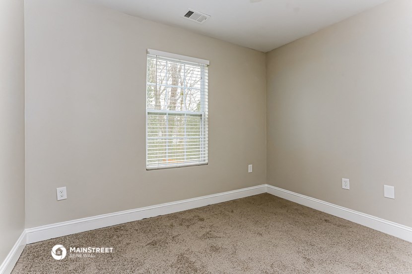 the bedroom of a house with carpet and a window