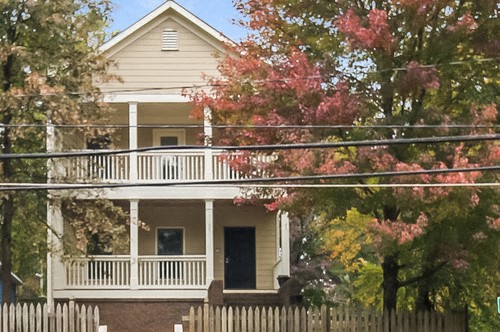 a yellow house with a white porch and a white fence
