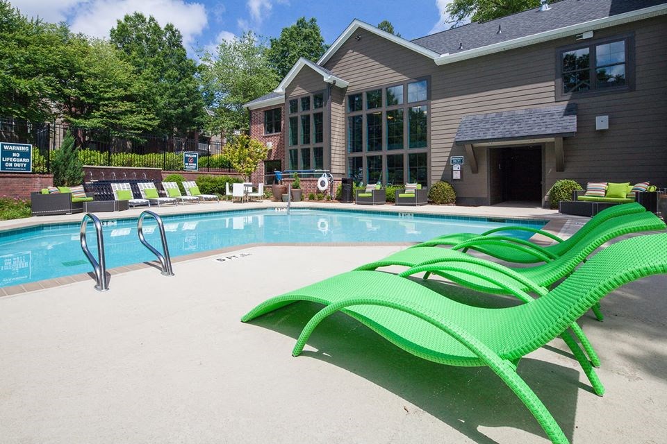 a swimming pool with green lounge chairs in front of a house